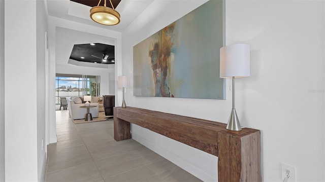 corridor featuring a tray ceiling and light tile patterned floors