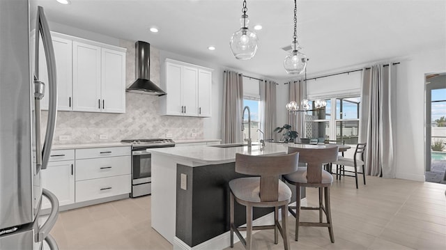 kitchen featuring sink, wall chimney exhaust hood, stainless steel appliances, pendant lighting, and a center island with sink