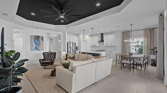 living room featuring ceiling fan with notable chandelier, a raised ceiling, and sink