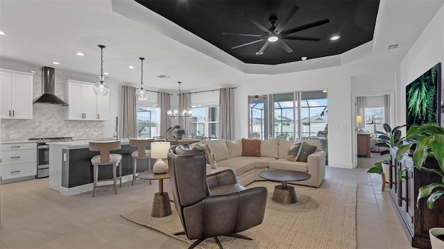 living room featuring a raised ceiling, light tile patterned floors, and ceiling fan with notable chandelier