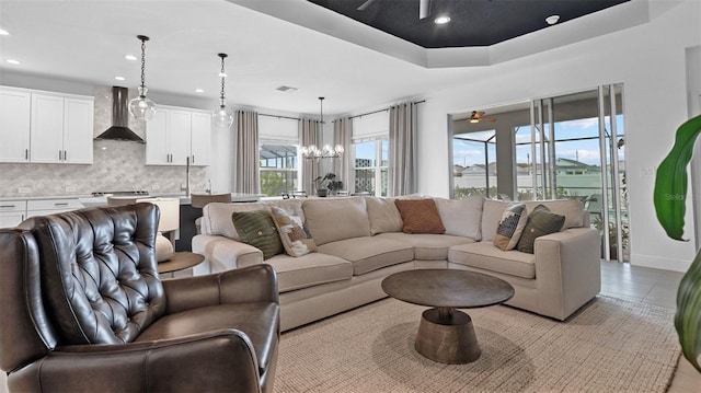 tiled living room with ceiling fan with notable chandelier and a raised ceiling