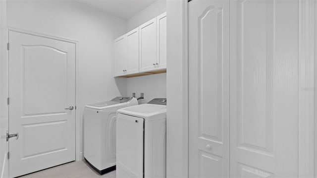 laundry room with washer and clothes dryer, light tile patterned flooring, and cabinets