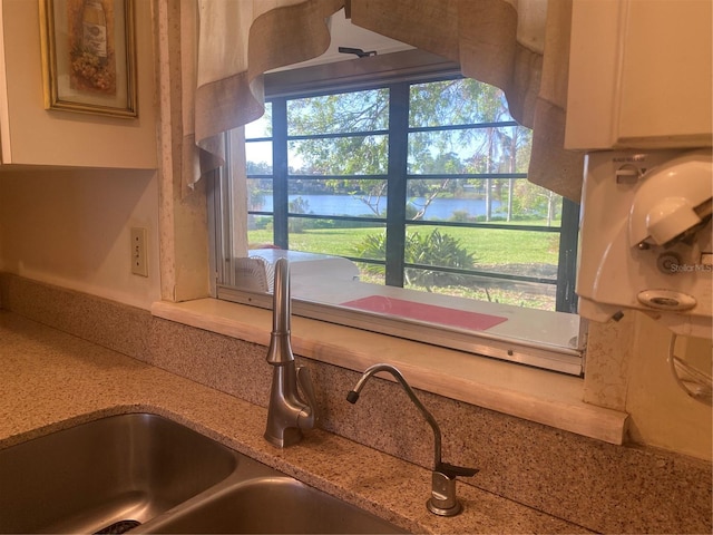 interior details with a water view, sink, and light stone counters