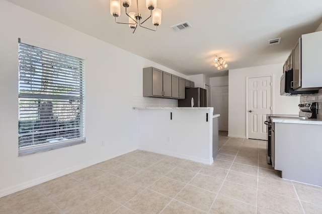 kitchen featuring stainless steel appliances, an inviting chandelier, gray cabinets, decorative backsplash, and light tile patterned floors