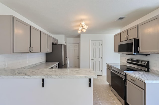 kitchen with kitchen peninsula, appliances with stainless steel finishes, backsplash, gray cabinetry, and light tile patterned floors