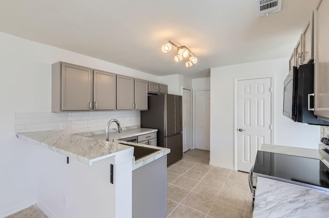 kitchen with stove, backsplash, gray cabinets, stainless steel fridge, and kitchen peninsula