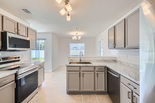 kitchen with decorative backsplash, kitchen peninsula, stainless steel appliances, sink, and an inviting chandelier