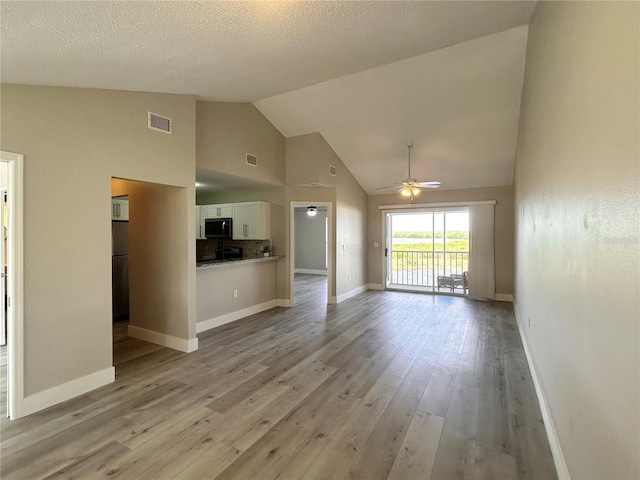 unfurnished living room featuring ceiling fan, lofted ceiling, a textured ceiling, and light hardwood / wood-style flooring