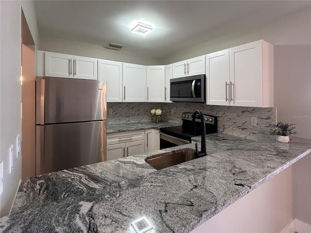 kitchen featuring tasteful backsplash, light stone counters, kitchen peninsula, white cabinets, and appliances with stainless steel finishes