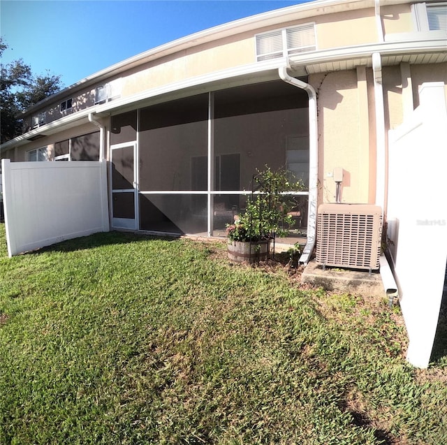 rear view of house with a sunroom, a lawn, and central AC unit