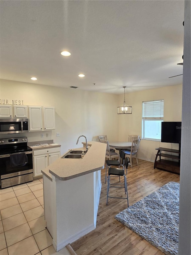 kitchen featuring pendant lighting, white cabinets, stainless steel appliances, an island with sink, and sink