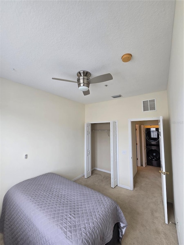 carpeted bedroom with stacked washer and dryer, ceiling fan, a closet, and a textured ceiling