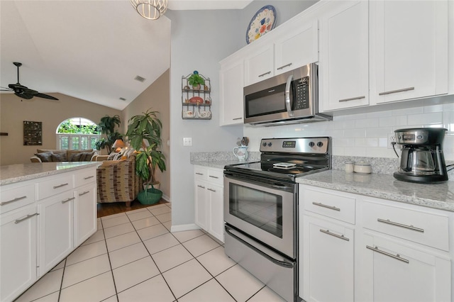 kitchen with light stone counters, stainless steel appliances, light tile patterned floors, white cabinetry, and lofted ceiling