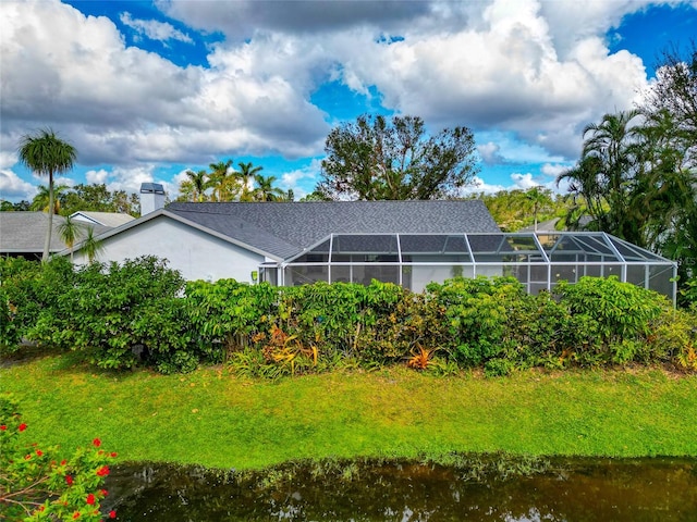 rear view of house with a lanai, a yard, and a water view