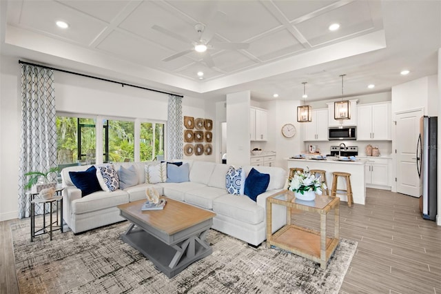 living room featuring light hardwood / wood-style floors, ceiling fan, beam ceiling, and coffered ceiling