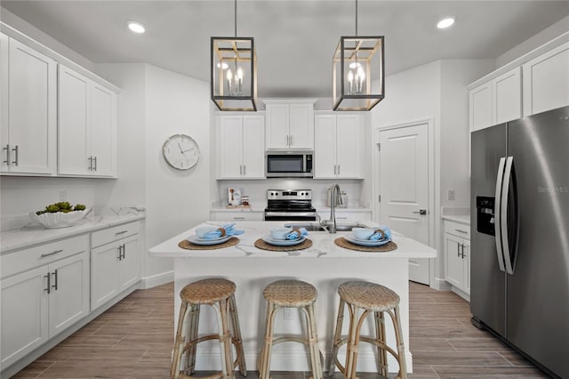 kitchen with light stone counters, light hardwood / wood-style flooring, a kitchen island with sink, white cabinetry, and appliances with stainless steel finishes