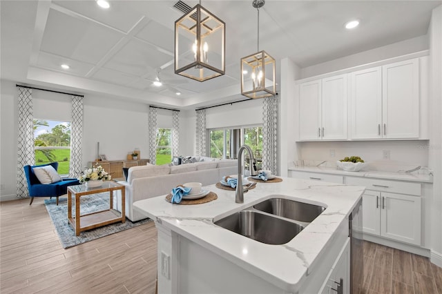 kitchen featuring white cabinets, a center island with sink, sink, and light wood-type flooring