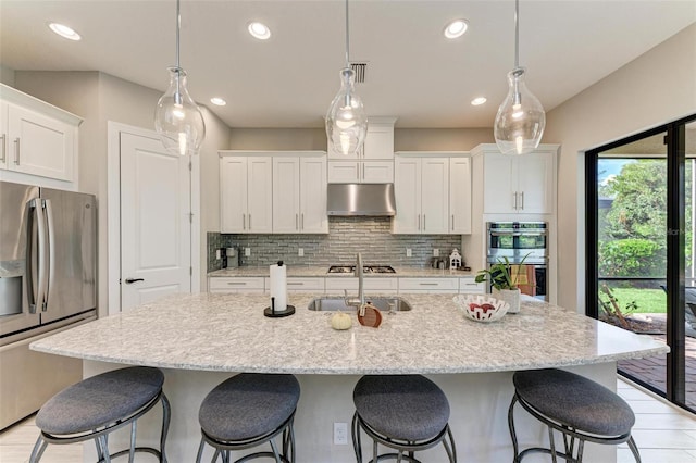 kitchen featuring range hood, white cabinets, a center island with sink, and stainless steel appliances