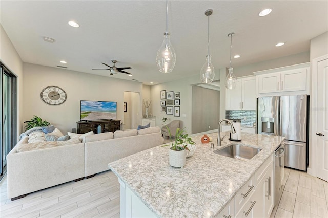 kitchen featuring a center island with sink, white cabinetry, appliances with stainless steel finishes, hanging light fixtures, and sink