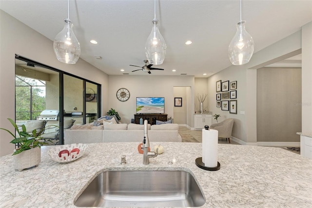 kitchen featuring ceiling fan, sink, decorative light fixtures, and light stone counters