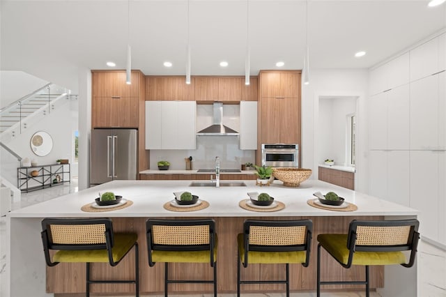 kitchen featuring stainless steel appliances, white cabinetry, decorative light fixtures, a kitchen bar, and wall chimney exhaust hood