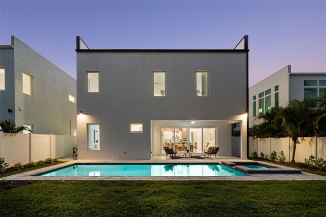 back house at dusk with a patio, a yard, and a swimming pool with hot tub