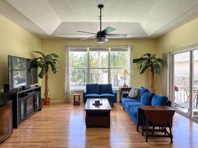 living room featuring a raised ceiling, ceiling fan, and light hardwood / wood-style floors