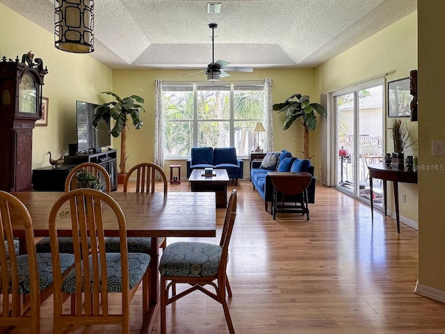 dining space with a raised ceiling, a wealth of natural light, ceiling fan, and light wood-type flooring