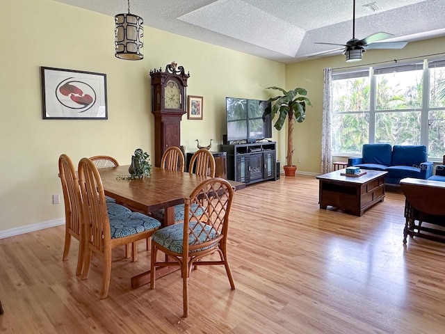 dining space with a textured ceiling, a tray ceiling, light hardwood / wood-style flooring, and ceiling fan