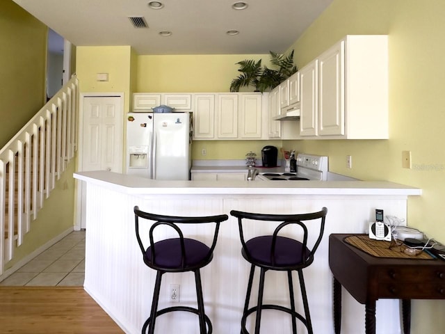 kitchen with kitchen peninsula, white appliances, white cabinets, light hardwood / wood-style floors, and a breakfast bar area