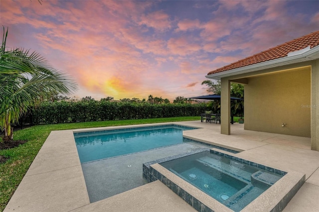 pool at dusk with an in ground hot tub and a patio area