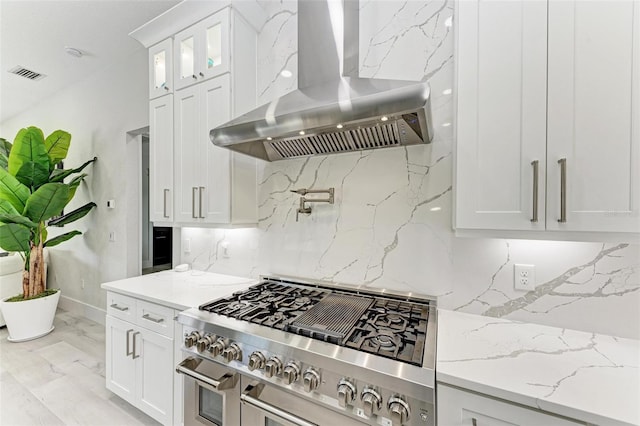 kitchen featuring light stone countertops, island exhaust hood, white cabinetry, and high end range