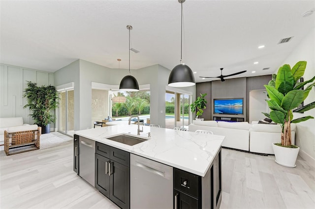 kitchen featuring light hardwood / wood-style floors, dishwasher, hanging light fixtures, sink, and an island with sink