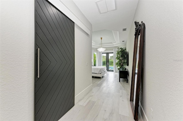 hallway with french doors, light wood-type flooring, a notable chandelier, and a tray ceiling