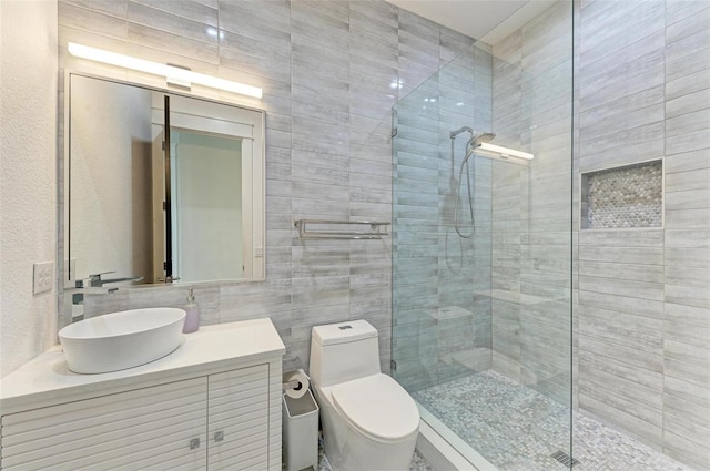 bathroom featuring tile walls, vanity, toilet, and a shower with shower door