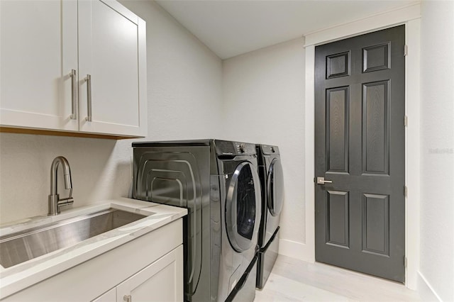 laundry area featuring cabinets, separate washer and dryer, light hardwood / wood-style flooring, and sink