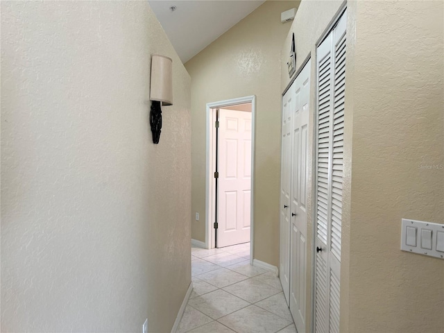 hallway featuring light tile patterned flooring and vaulted ceiling