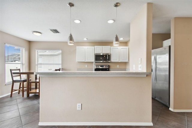 kitchen featuring white cabinets, dark tile patterned flooring, stainless steel appliances, and pendant lighting