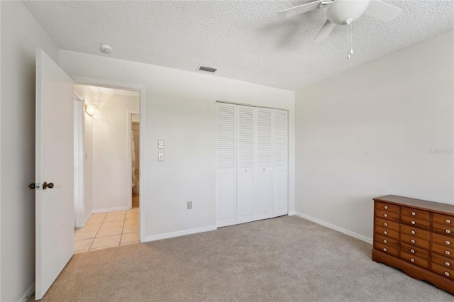 unfurnished bedroom with a textured ceiling, light carpet, ceiling fan, and a closet