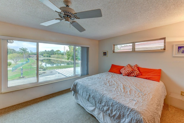 carpeted bedroom with a water view, multiple windows, a textured ceiling, and ceiling fan