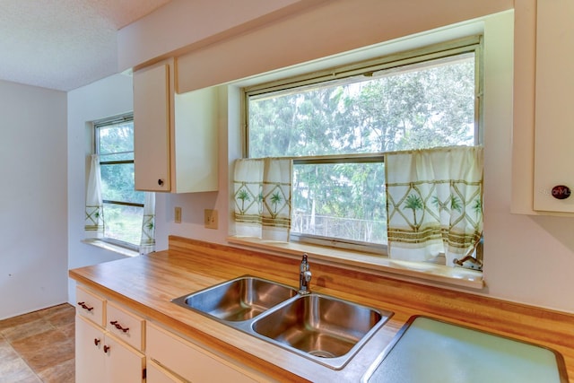 kitchen featuring white cabinets, a textured ceiling, sink, and butcher block countertops