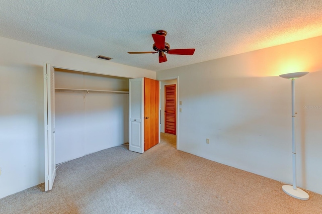 unfurnished bedroom featuring ceiling fan, a textured ceiling, light carpet, and a closet