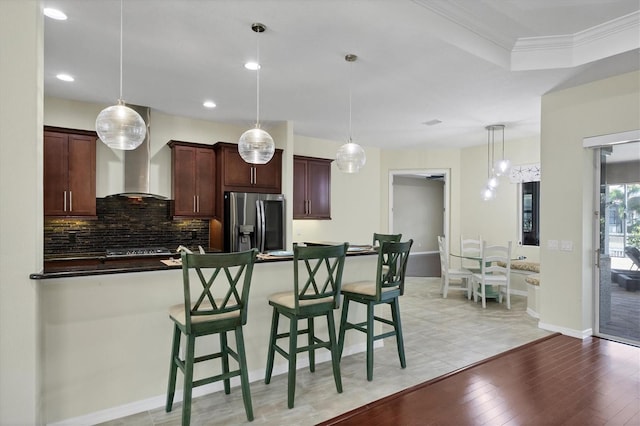 kitchen featuring dark brown cabinets, crown molding, pendant lighting, light hardwood / wood-style flooring, and stainless steel fridge with ice dispenser