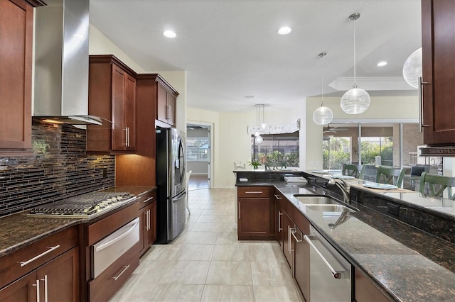 kitchen featuring sink, wall chimney exhaust hood, hanging light fixtures, dark stone countertops, and appliances with stainless steel finishes