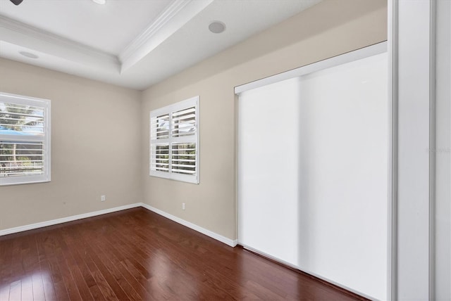 unfurnished bedroom featuring dark hardwood / wood-style floors, a raised ceiling, ornamental molding, and a closet