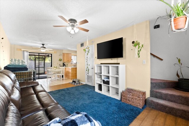 living room with ceiling fan, light wood-type flooring, and a textured ceiling