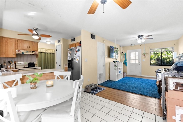 kitchen featuring white electric range, stainless steel refrigerator with ice dispenser, decorative backsplash, range hood, and light hardwood / wood-style floors