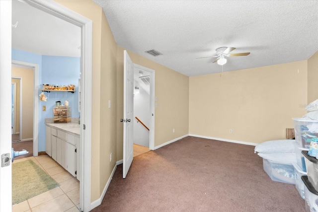 interior space with a textured ceiling, light colored carpet, and ceiling fan