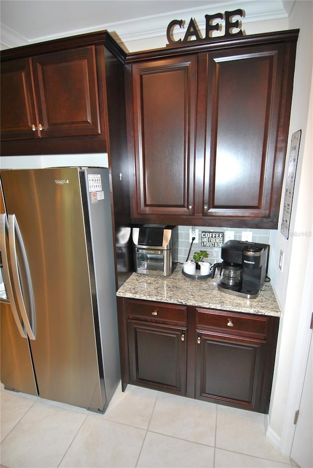 kitchen with ornamental molding, light tile patterned floors, light stone counters, and stainless steel refrigerator