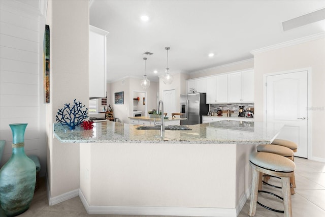 kitchen with kitchen peninsula, stainless steel refrigerator with ice dispenser, light stone counters, sink, and white cabinetry